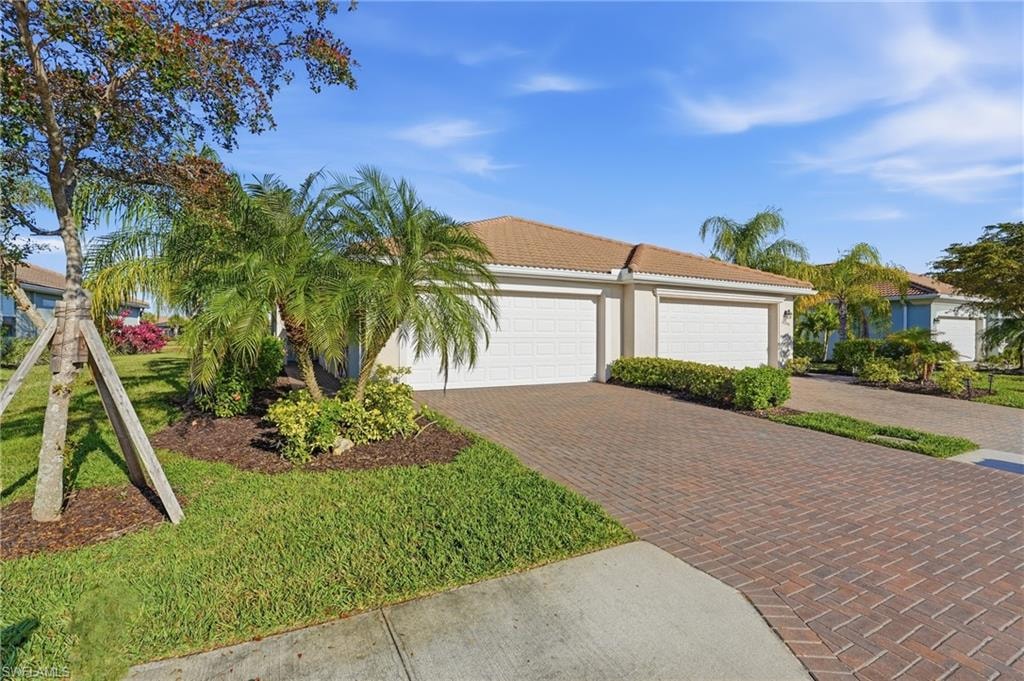 Ranch-style home with a tile roof, decorative driveway, a front lawn, stucco siding, and a garage