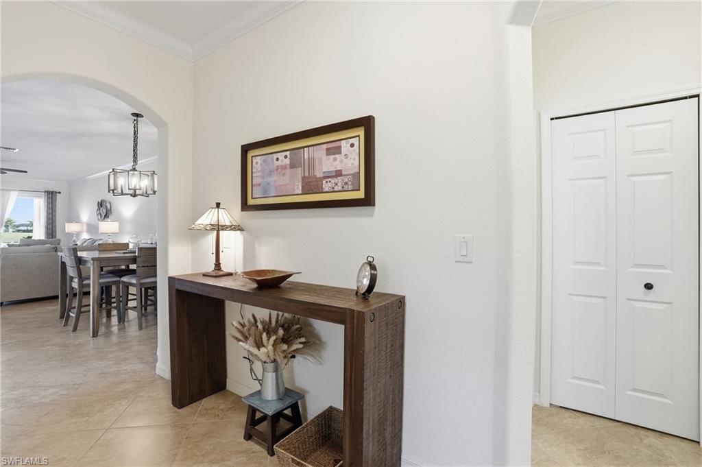 Hall featuring ornamental molding, arched walkways, light tile patterned floors, and a chandelier