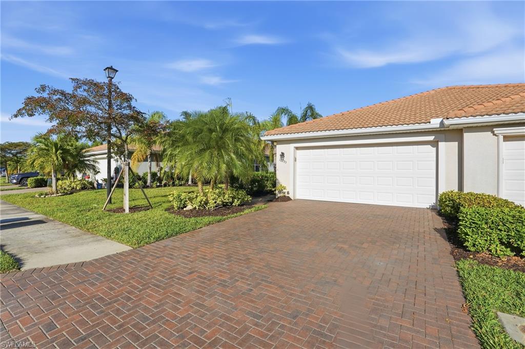 View of front of property featuring a garage, a front lawn, stucco siding, a tile roof, and decorative driveway