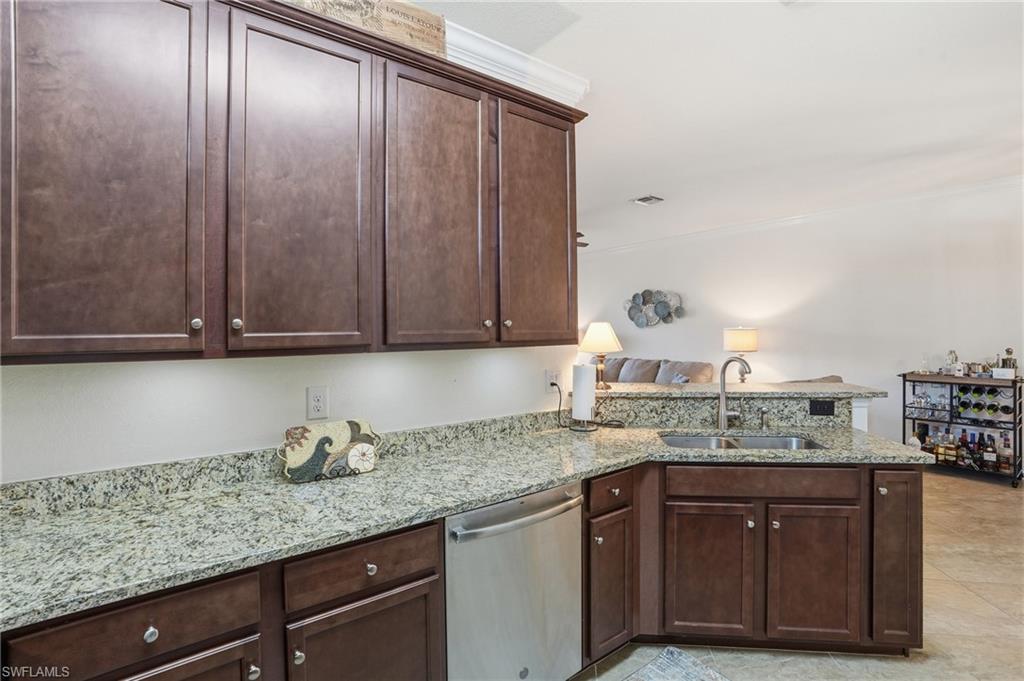 Kitchen with a peninsula, dark brown cabinets, stainless steel dishwasher, light stone countertops, and ornamental molding