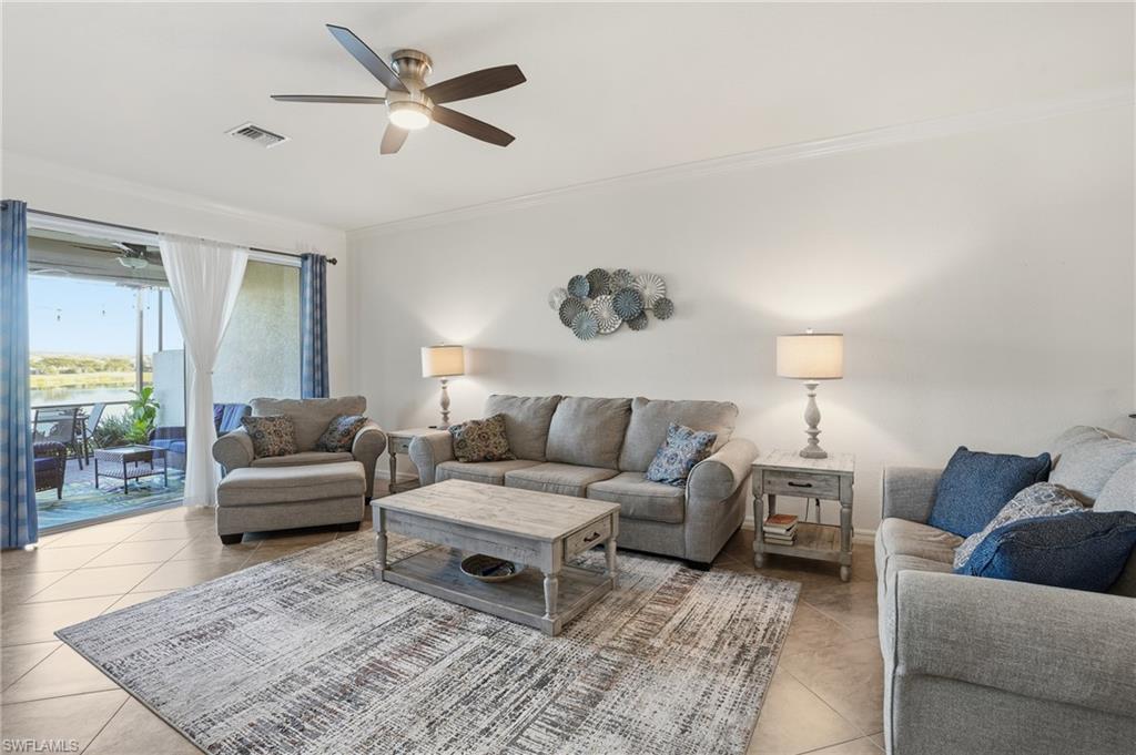 Living area with a water view, ornamental molding, ceiling fan, and light tile patterned floors
