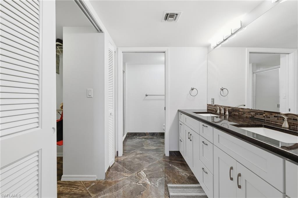 Full bathroom featuring double vanity, dark marble finish floors, a shower with shower door, and a walk in closet