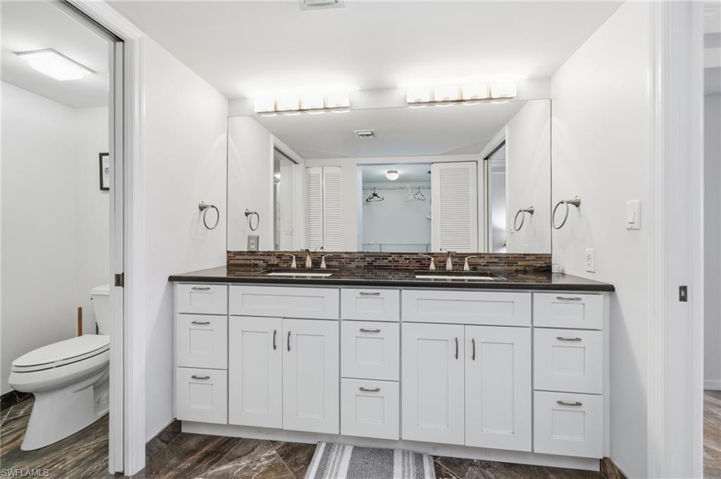 Bathroom with double vanity, a closet, backsplash, and dark marble finish floors