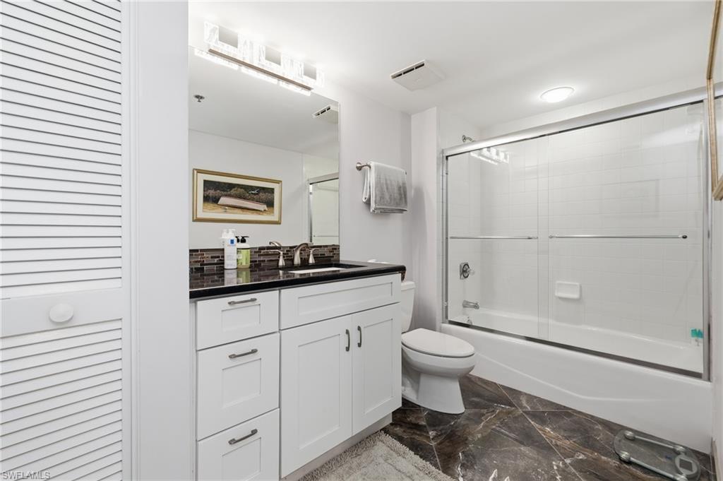 Bathroom featuring a closet, vanity, shower / bath combination with glass door, and dark marble finish flooring