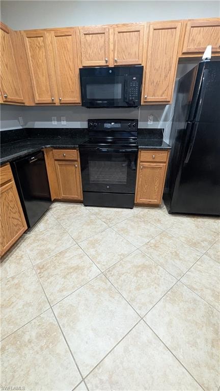 Kitchen featuring black appliances, brown cabinetry, dark stone counters, and light tile patterned flooring