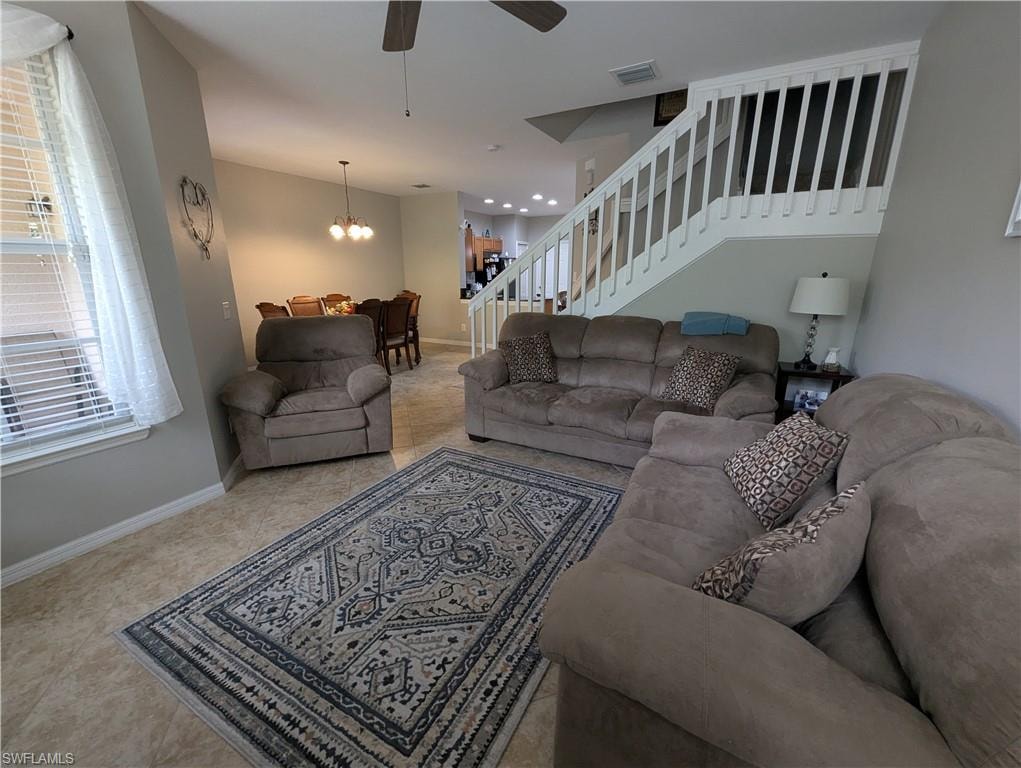 Living room with stairway, a ceiling fan, a chandelier, and light tile patterned floors