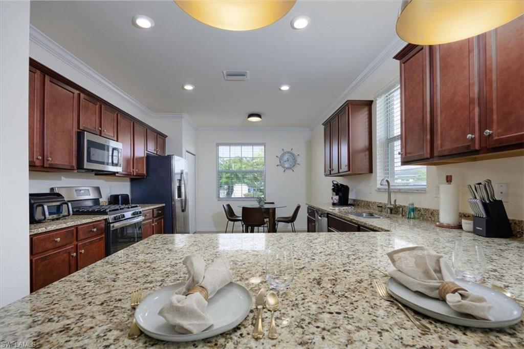 Kitchen featuring ornamental molding, light stone countertops, appliances with stainless steel finishes, and recessed lighting