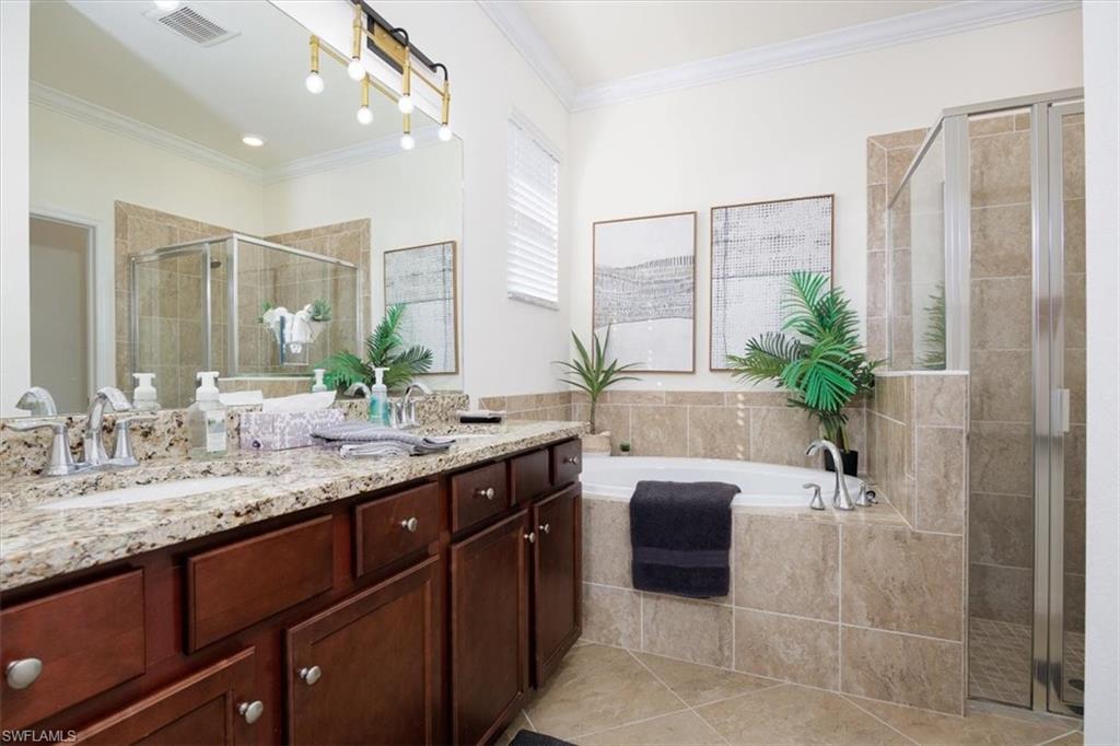 Full bathroom with double vanity, a garden tub, ornamental molding, a stall shower, and light tile patterned floors