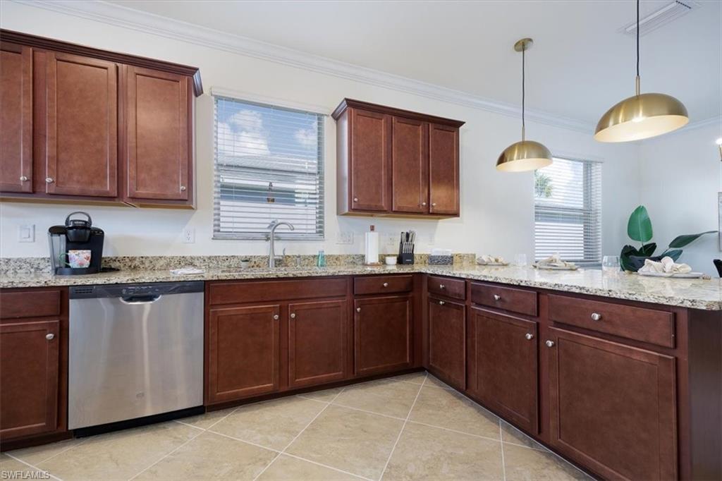 Large Kitchen featuring stainless steel dishwasher, ornamental molding, light stone countertops, pendant lighting, and light tile patterned flooring