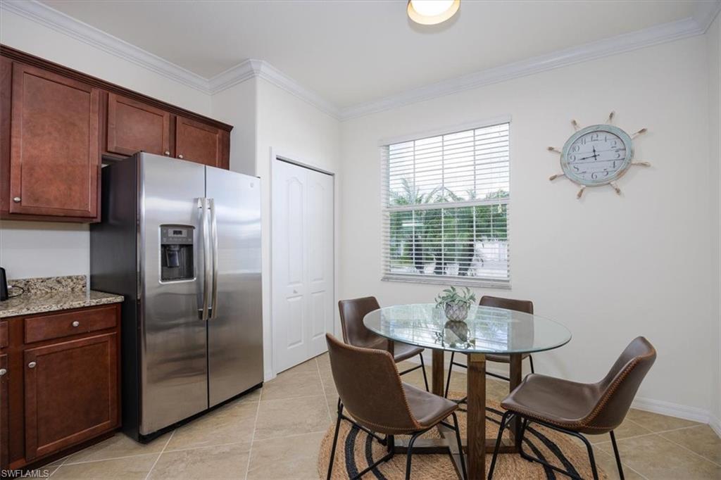 Eat in Kitchen featuring stainless steel fridge, crown molding, dark brown cabinets, light stone countertops, and light tile patterned floors
