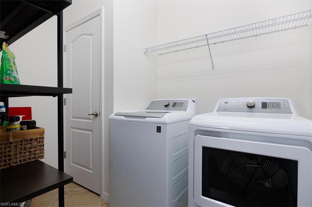 Washroom with washing machine and dryer and light tile patterned flooring