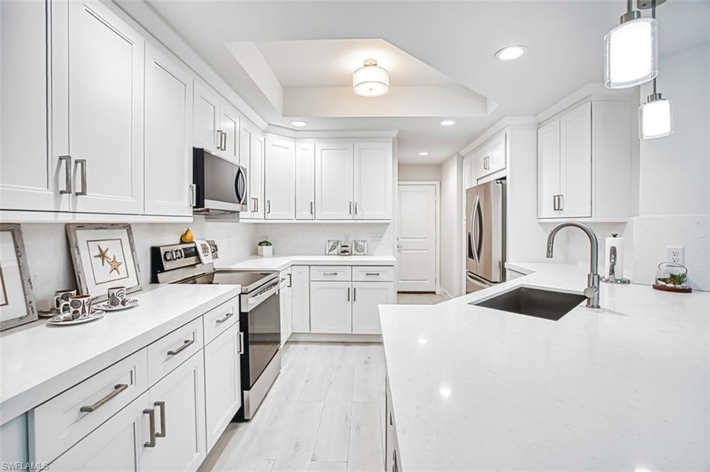 Kitchen with stainless steel appliances, light stone countertops, hanging light fixtures, a tray ceiling, and white cabinets