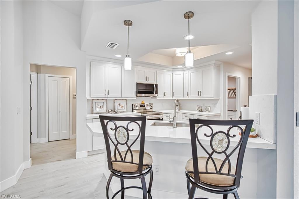 Kitchen featuring white cabinets, pendant lighting, a kitchen breakfast bar, stainless steel appliances, and light wood-style flooring