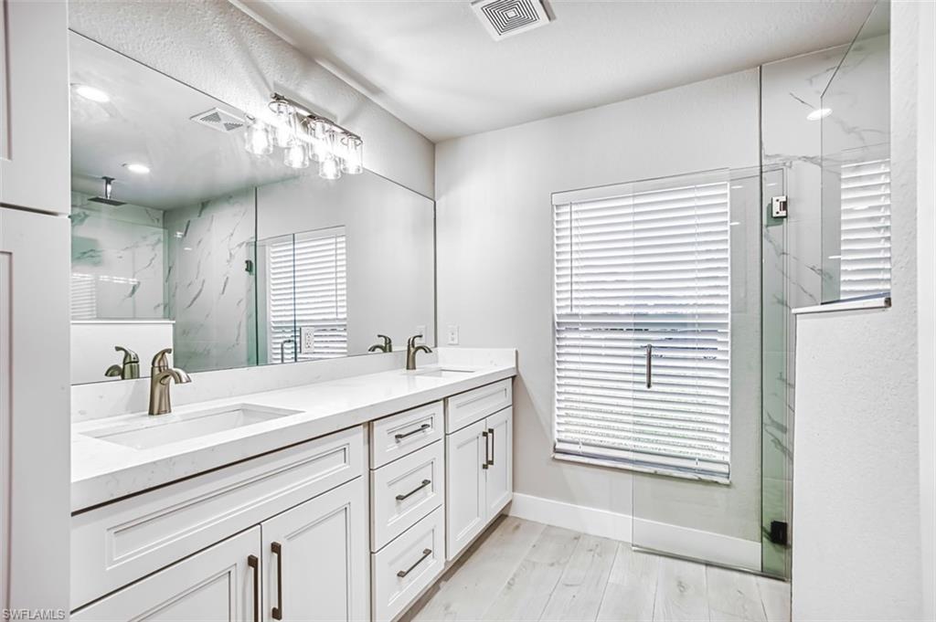Full bath with a marble finish shower, double vanity, and light wood-style floors