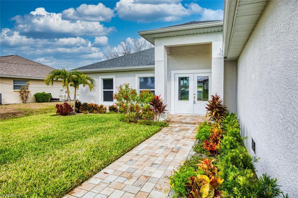 Property entrance with stucco siding, french doors, a lawn, and roof with shingles
