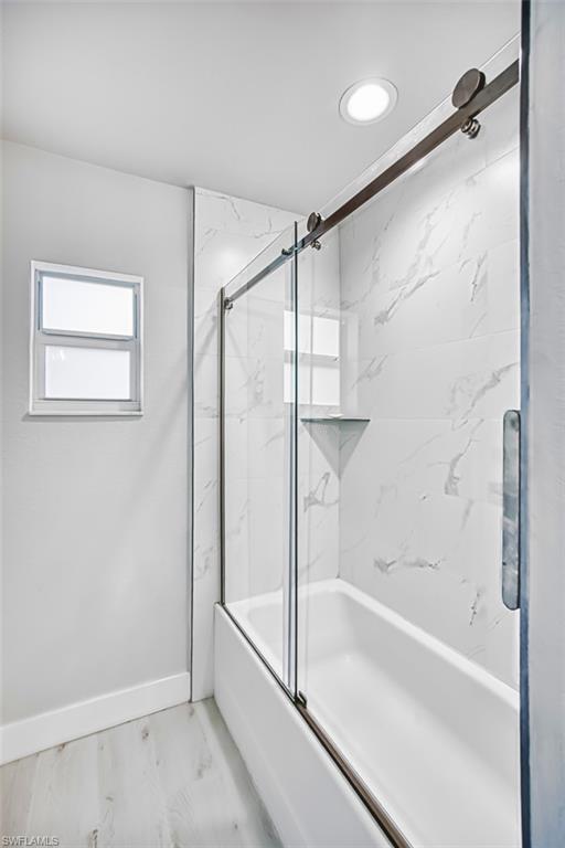 Bathroom featuring combined bath / shower with glass door and baseboards