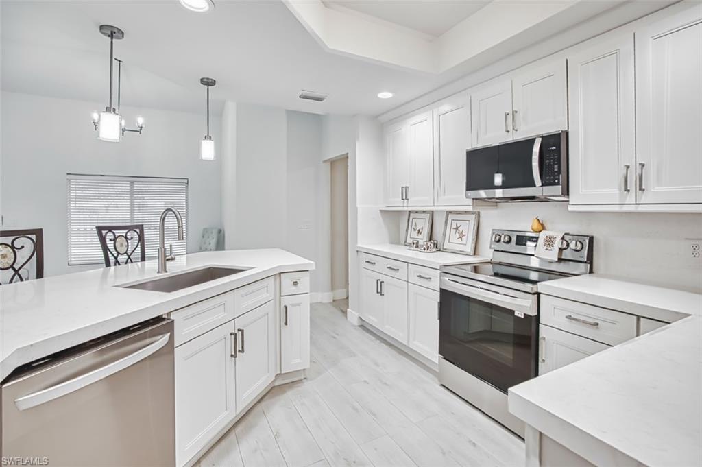 Kitchen featuring appliances with stainless steel finishes, white cabinetry, decorative light fixtures, recessed lighting, and light wood-style flooring