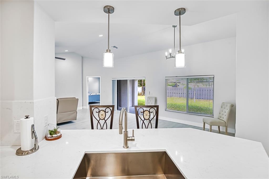 Kitchen featuring light stone counters, decorative light fixtures, wood finished floors, open floor plan, and vaulted ceiling