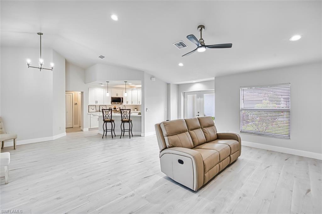 Living room featuring light wood-style floors, vaulted ceiling, a ceiling fan, recessed lighting, and a chandelier