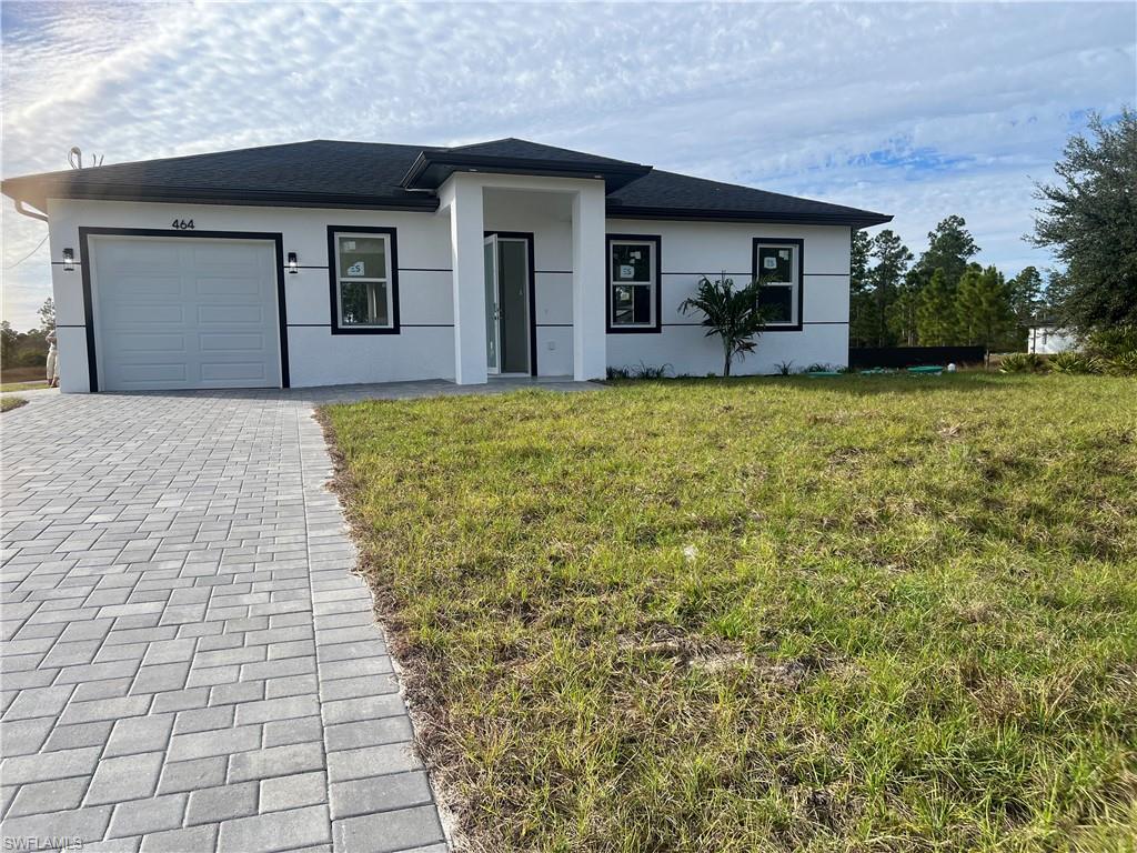 View of front of property with a front lawn, a garage, decorative driveway, stucco siding, and roof with shingles