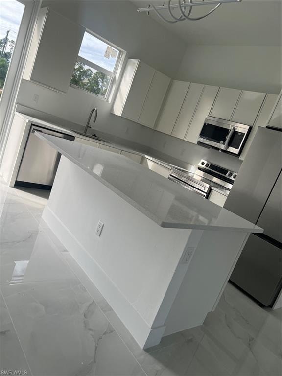Kitchen featuring light marble finish flooring, a kitchen island, white cabinets, and refrigerator