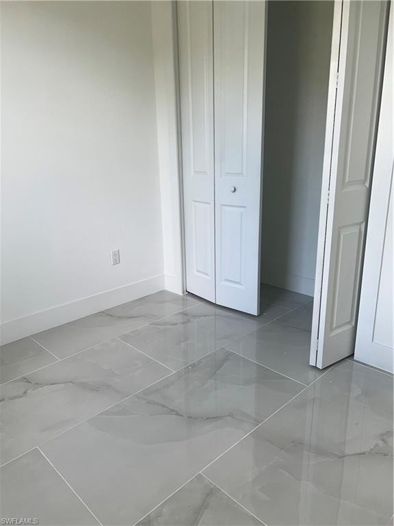 Unfurnished bedroom featuring marble finish floors and a closet