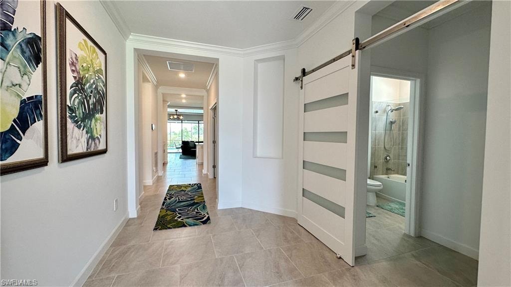 Hall featuring a barn door, crown molding, and light tile flooring