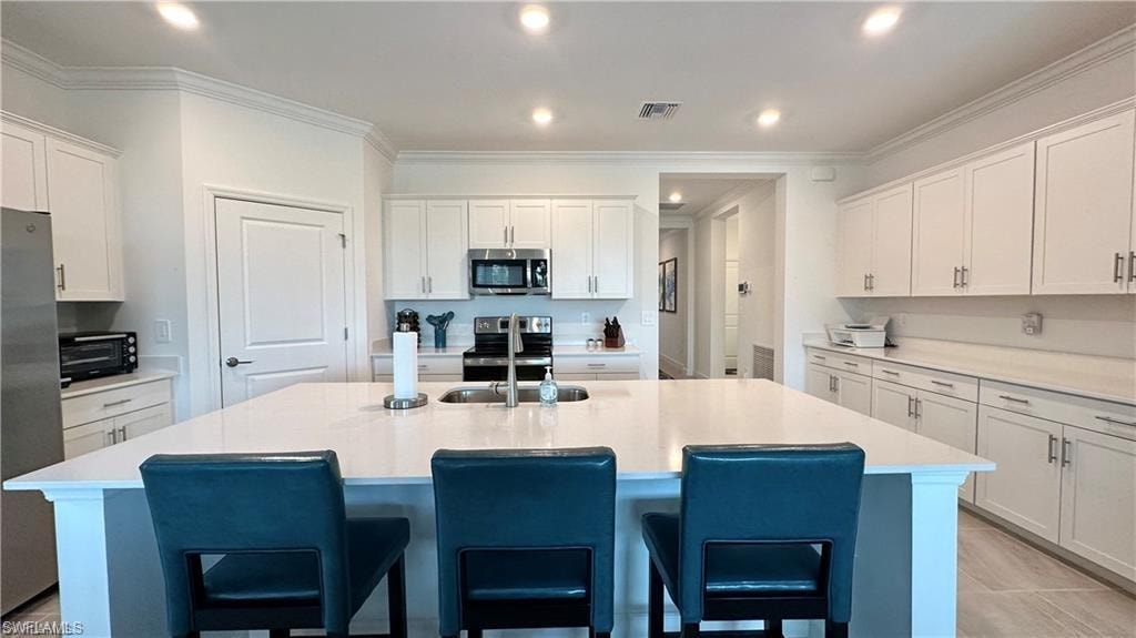 Kitchen with stainless steel appliances, a center island with sink, sink, and white cabinetry