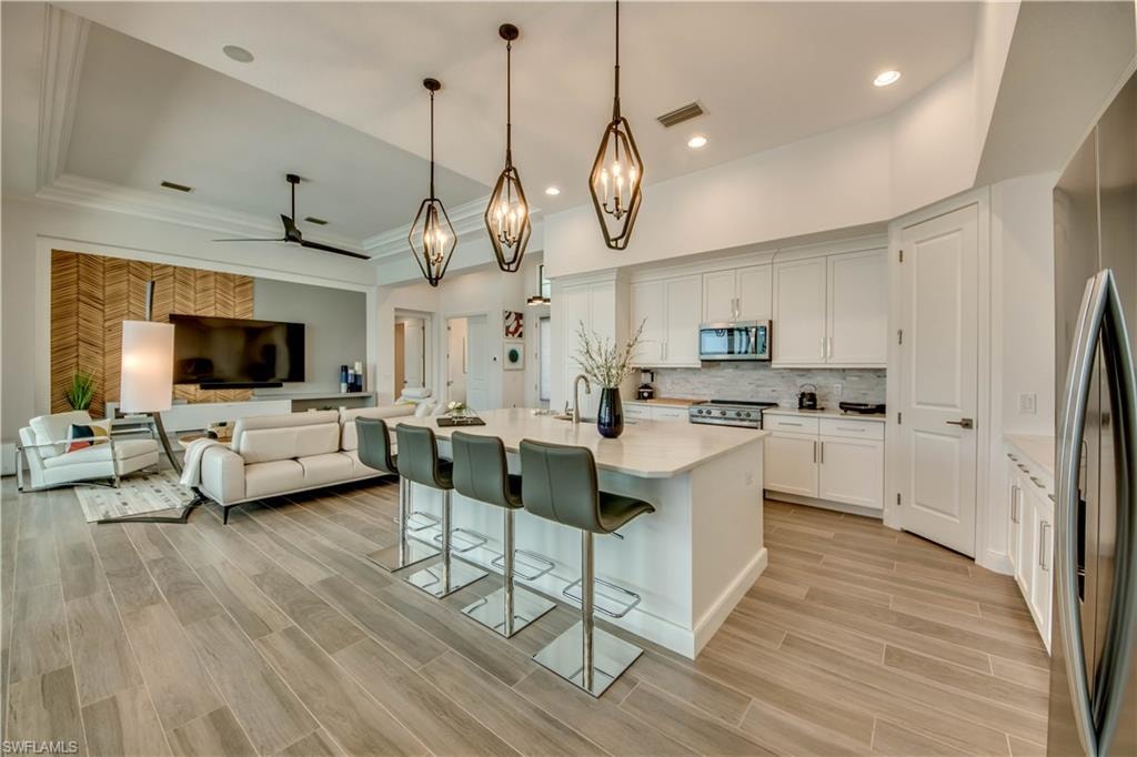Kitchen featuring appliances with stainless steel finishes, a kitchen bar, white cabinetry, decorative light fixtures, and recessed lighting