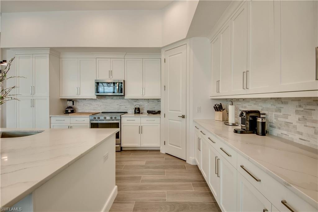 Kitchen with a kitchen breakfast bar, stainless steel appliances, white cabinetry, wood finish floors, and a kitchen island with sink