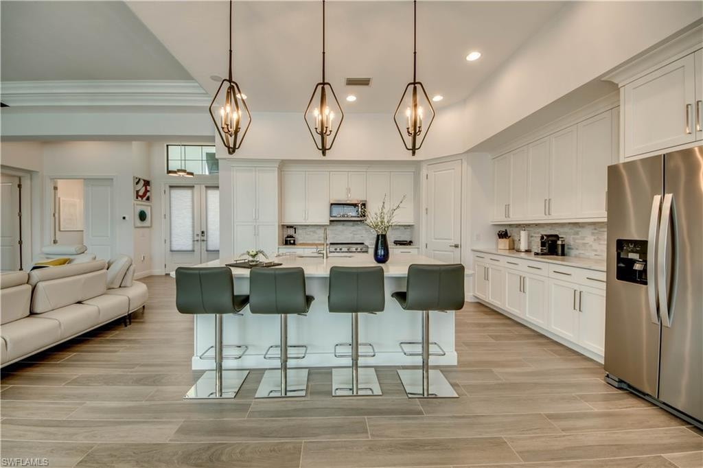 Kitchen with appliances with stainless steel finishes, a kitchen bar, white cabinets, wood finish floors, and decorative light fixtures