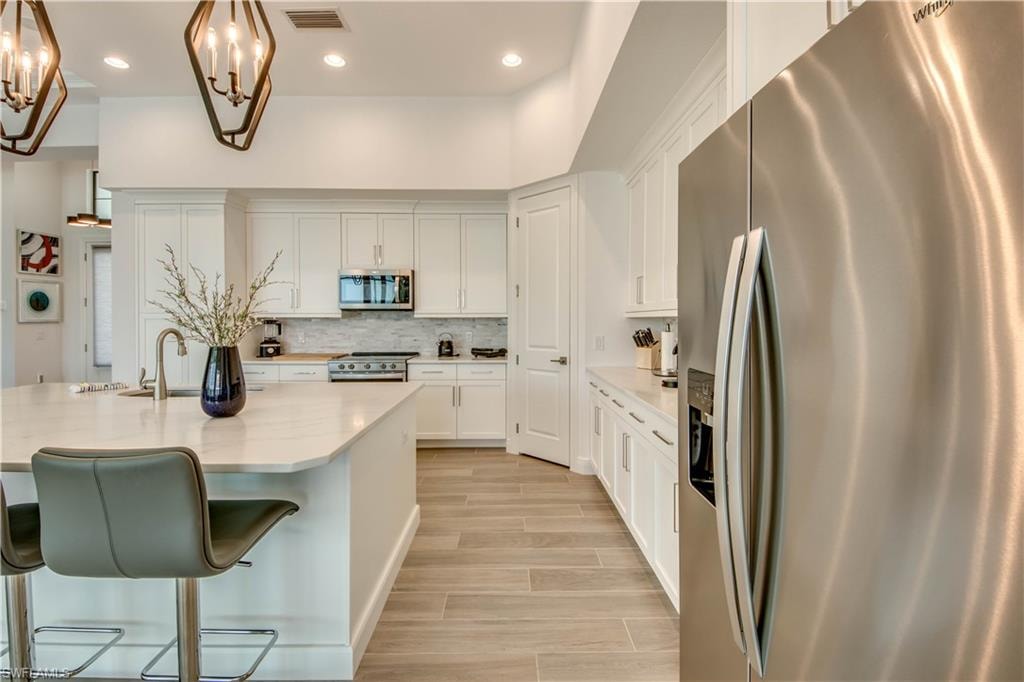 Kitchen with appliances with stainless steel finishes, light stone counters, white cabinetry, wood finish floors, and decorative backsplash