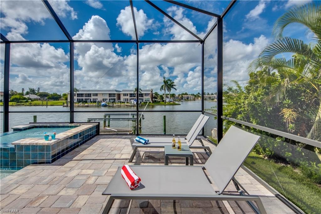 View of pool with a pool with connected hot tub, a water view, a sunroom, a patio area, and glass enclosure