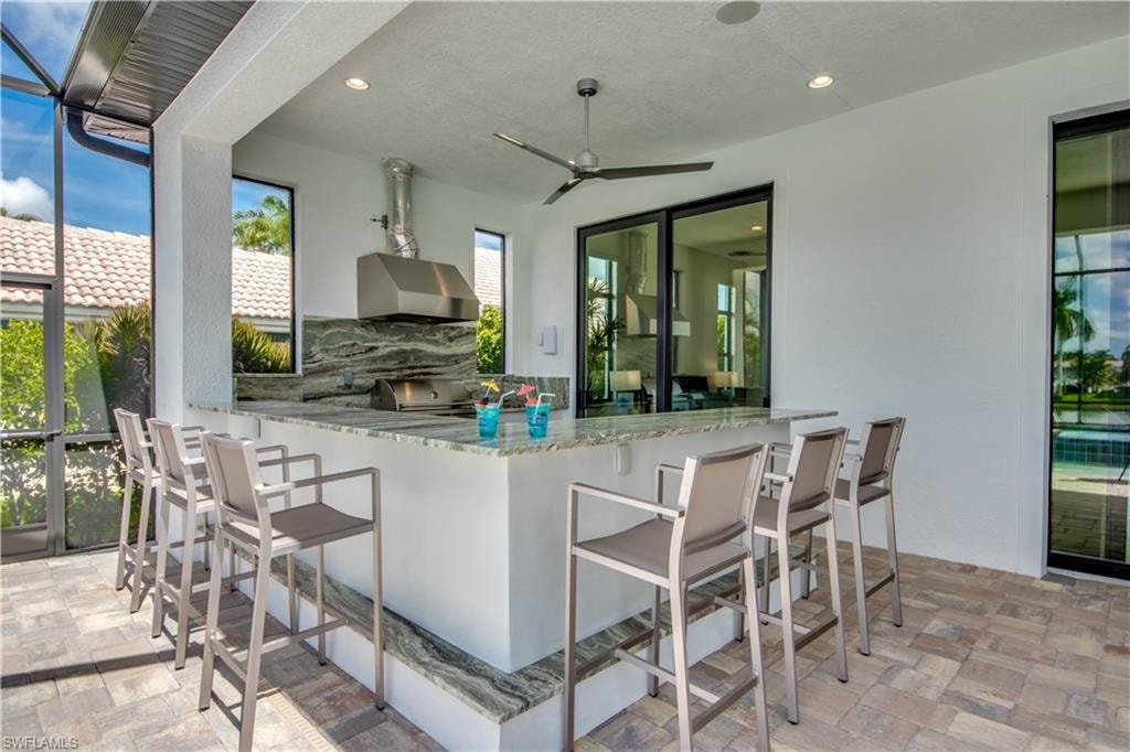 View of patio featuring exterior kitchen, a sunroom, glass enclosure, and a ceiling fan