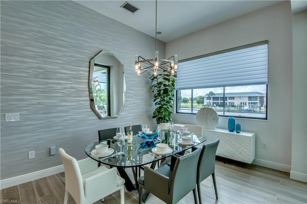 Dining room with wood tiled floors, a chandelier, a water view, and a sunroom