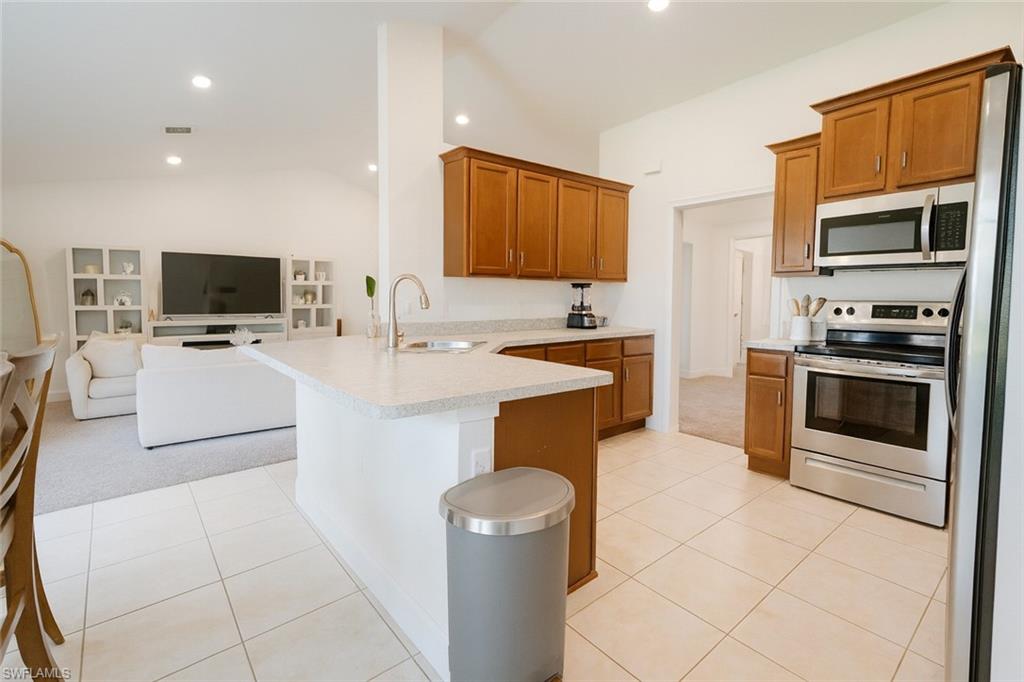 Kitchen with vaulted ceiling, a peninsula, brown cabinetry, appliances with stainless steel finishes, and light countertops