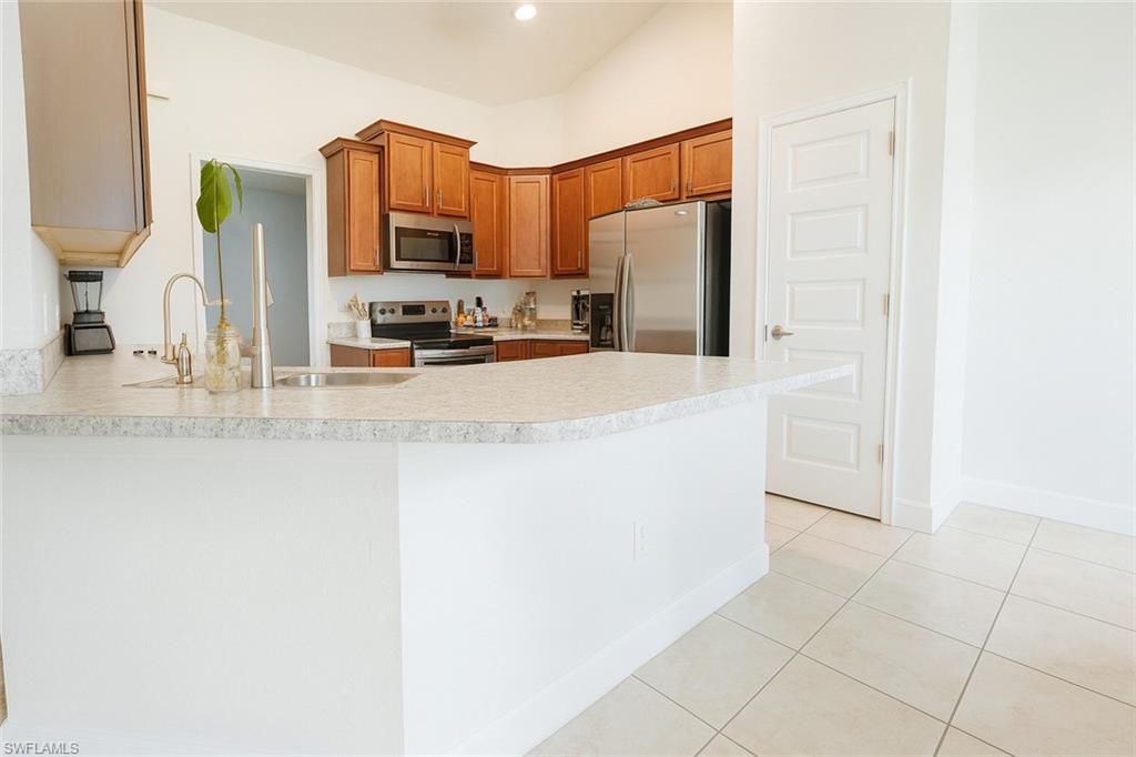 Kitchen with brown cabinetry, appliances with stainless steel finishes, light countertops, a peninsula, and light tile patterned floors