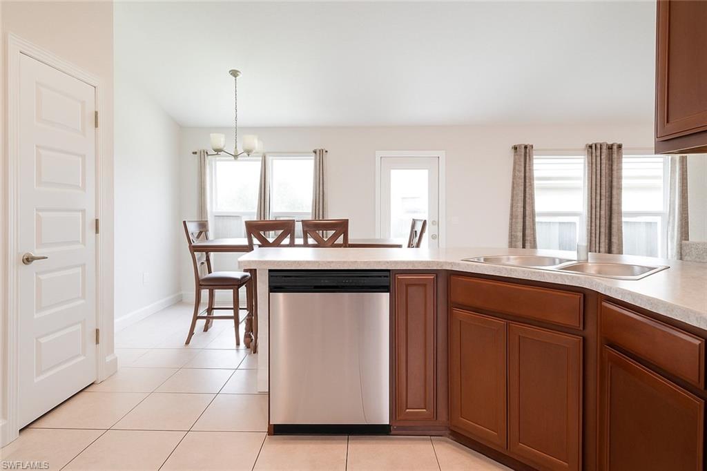 Kitchen featuring stainless steel dishwasher, light countertops, a peninsula, a chandelier, and brown cabinetry