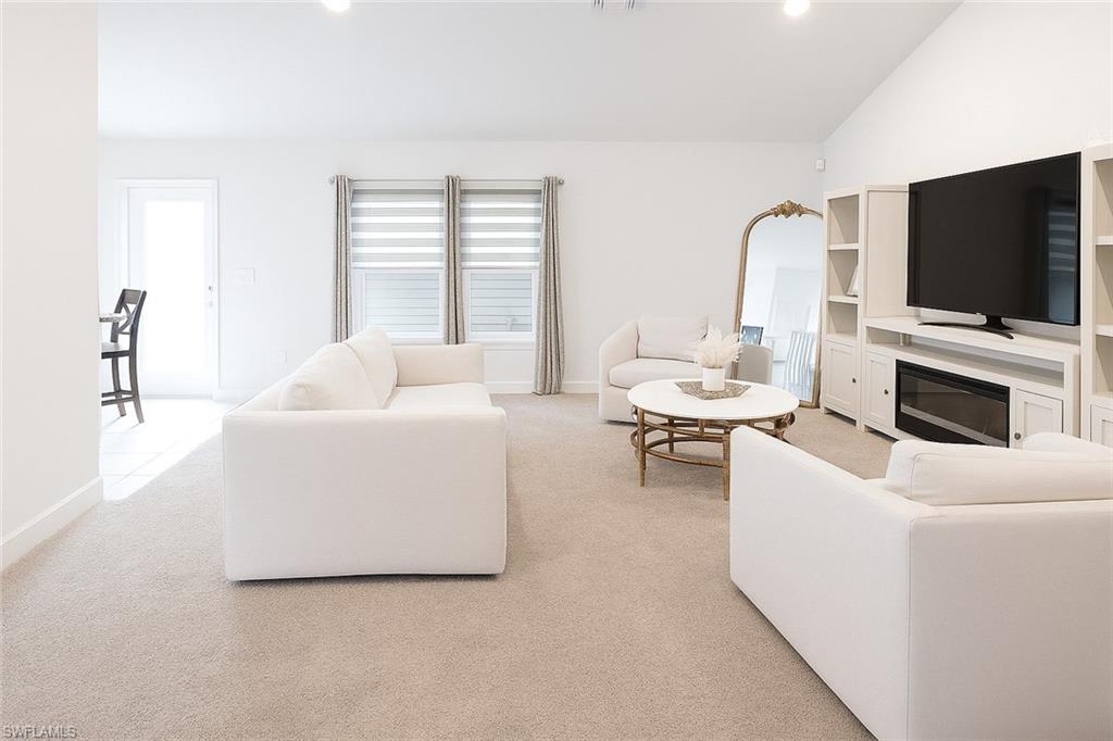 Living area with lofted ceiling, light colored carpet, a glass covered fireplace, recessed lighting, and arched walkways