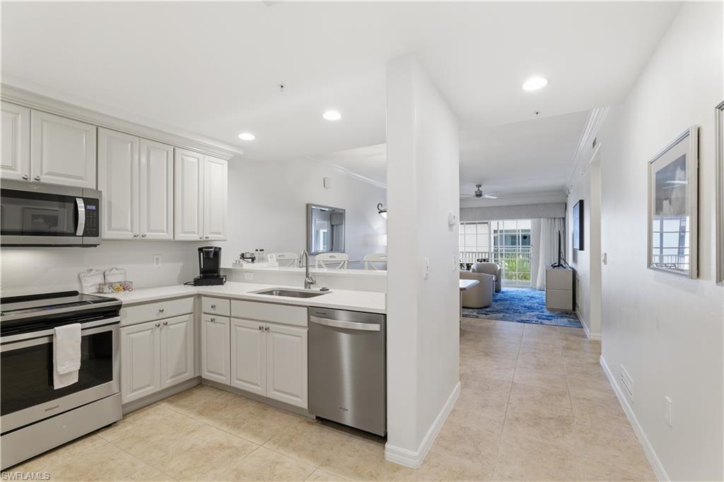 Kitchen with appliances with stainless steel finishes, open floor plan, light tile patterned floors, crown molding, and white cabinetry