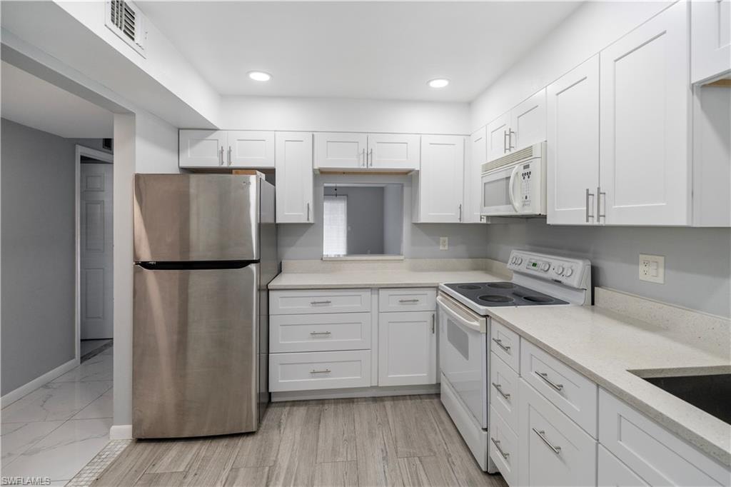 Kitchen featuring white appliances, white cabinetry, light stone counters, recessed lighting, and light wood-type flooring