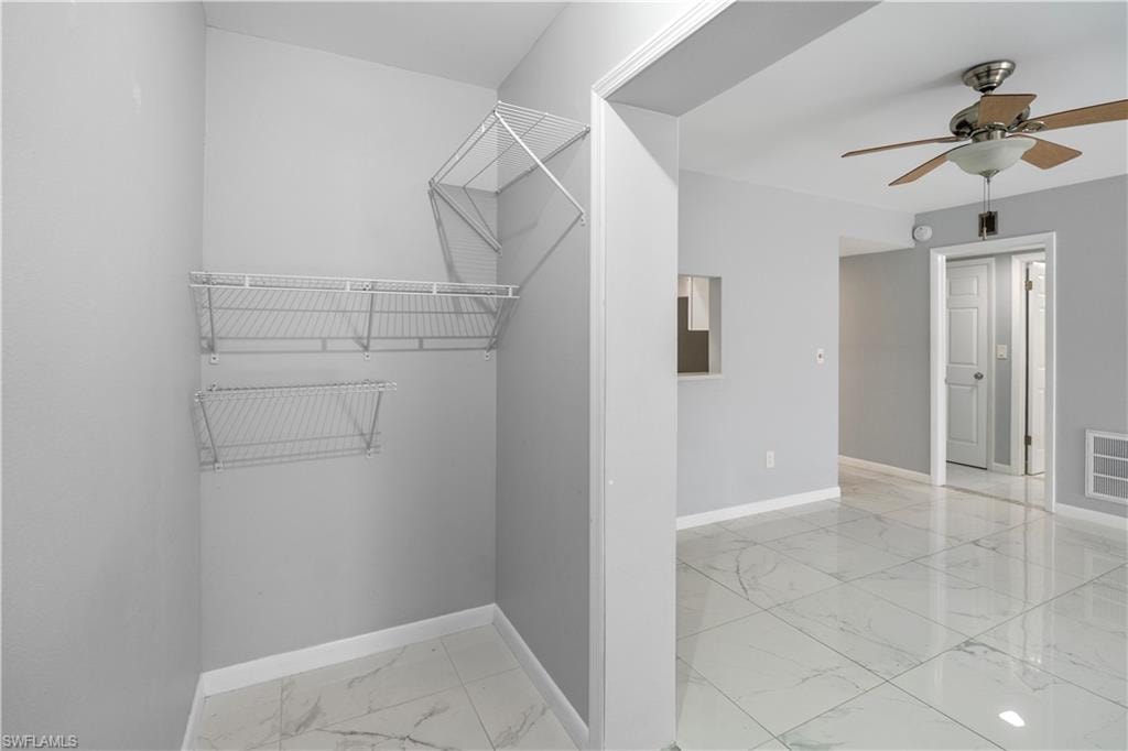 Spacious closet featuring light marble finish flooring and a ceiling fan