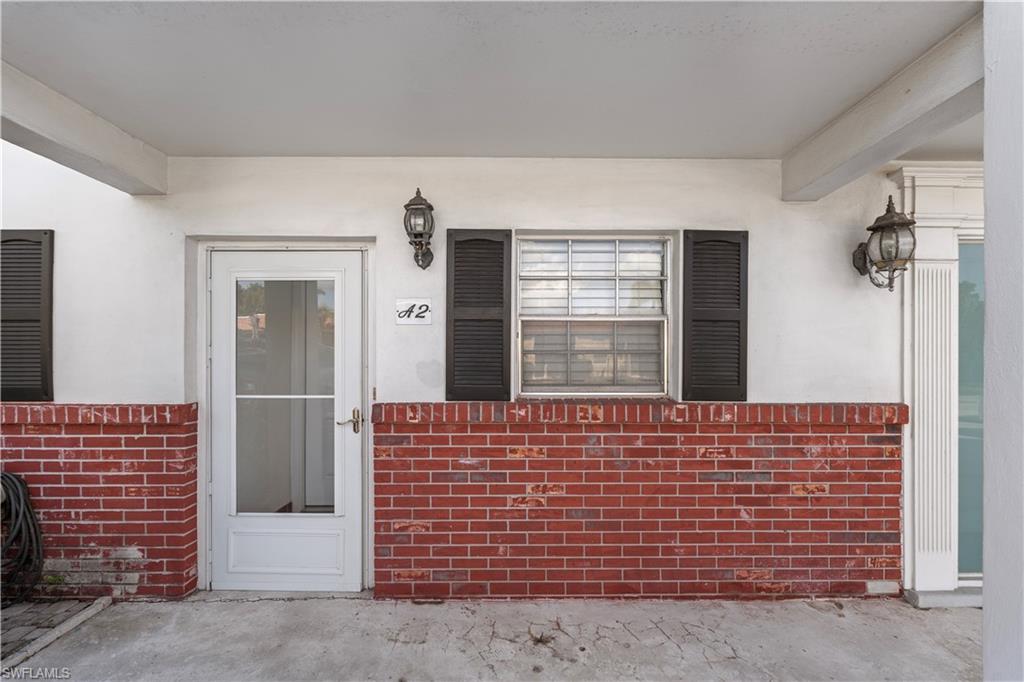 View of exterior entry featuring covered porch, stucco siding, and brick siding