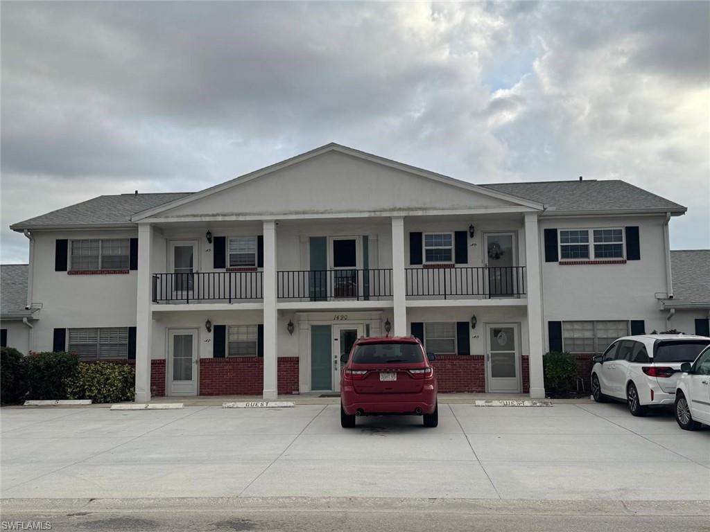 View of front of house with stucco siding, brick siding, uncovered parking, a balcony, and roof with shingles