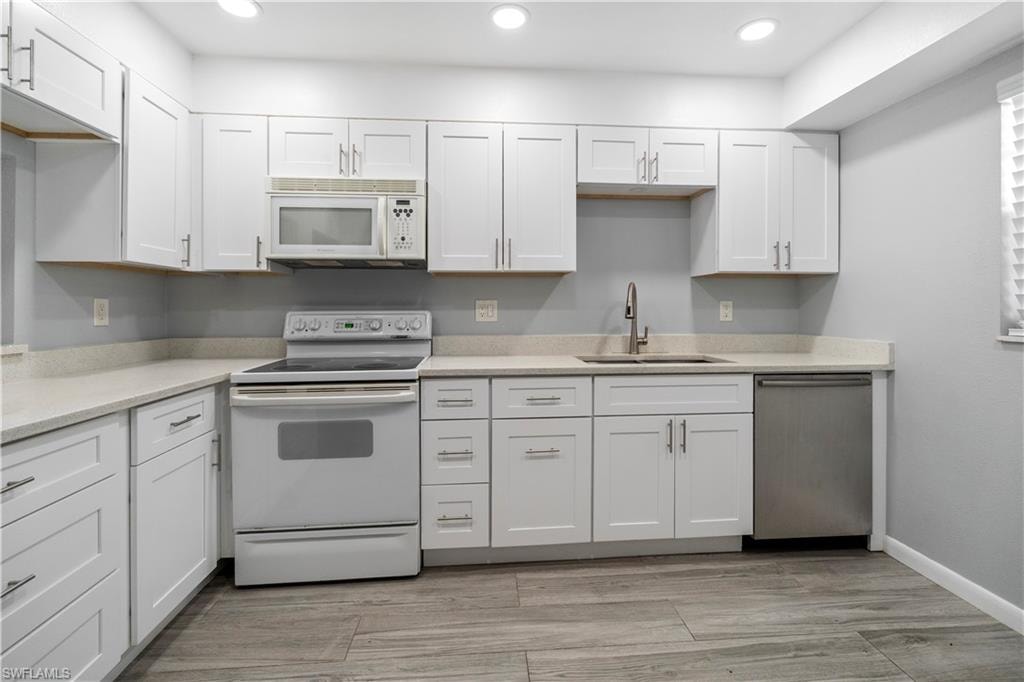 Kitchen featuring white appliances, white cabinetry, light stone counters, recessed lighting, and light wood-style flooring