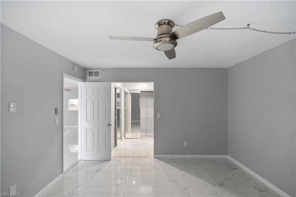 Unfurnished bedroom featuring light marble finish flooring, a ceiling fan, and a spacious closet