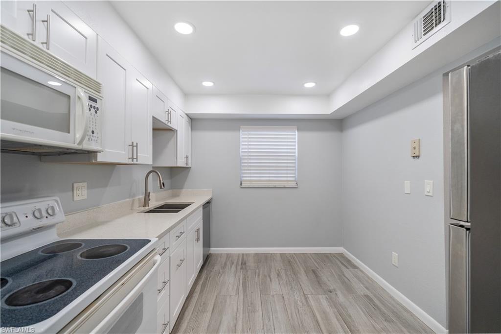 Kitchen with appliances with stainless steel finishes, white cabinetry, recessed lighting, light wood-type flooring, and light stone countertops