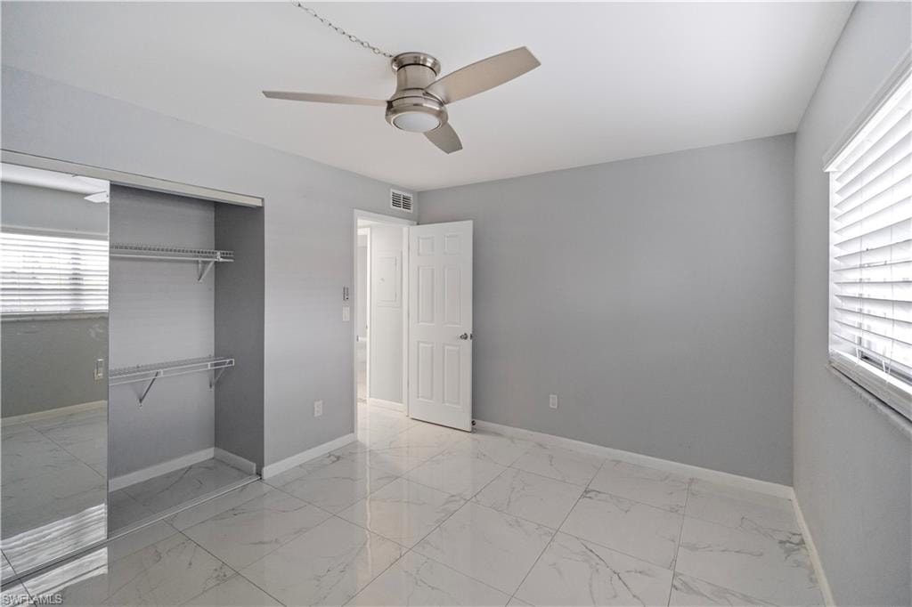 Unfurnished bedroom with light marble finish flooring, a ceiling fan, and a closet