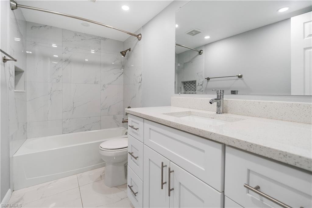 Bathroom featuring vanity, a combined bath / shower with marble appearance, light marble finish flooring, and recessed lighting
