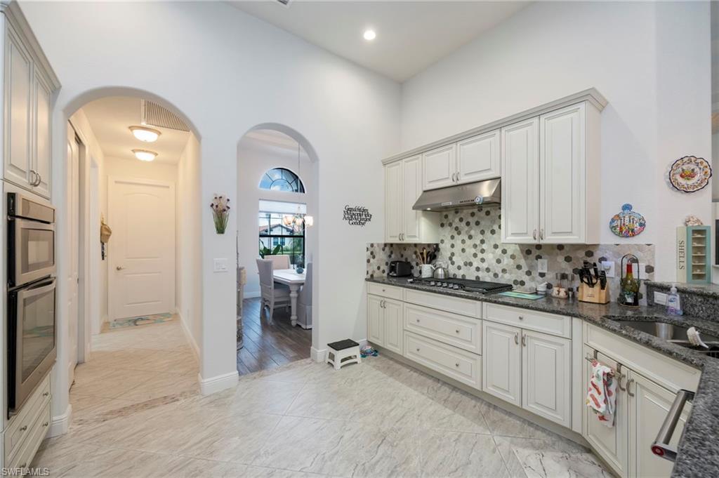 Kitchen featuring arched walkways, dark stone countertops, appliances with stainless steel finishes, under cabinet range hood, and backsplash